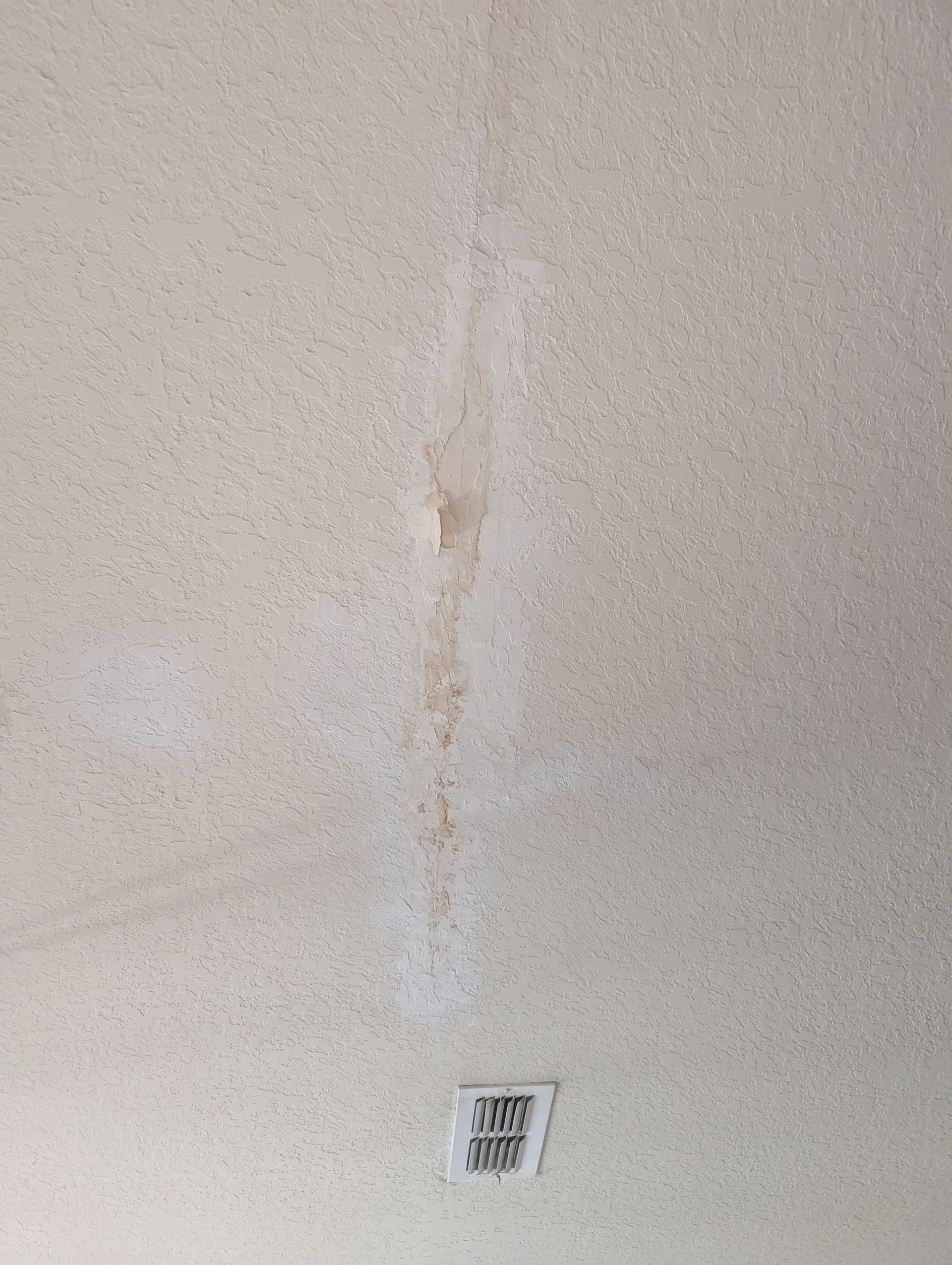 Water-stained, textured ceiling with a long, dark brown streak. A vent is visible at the bottom.