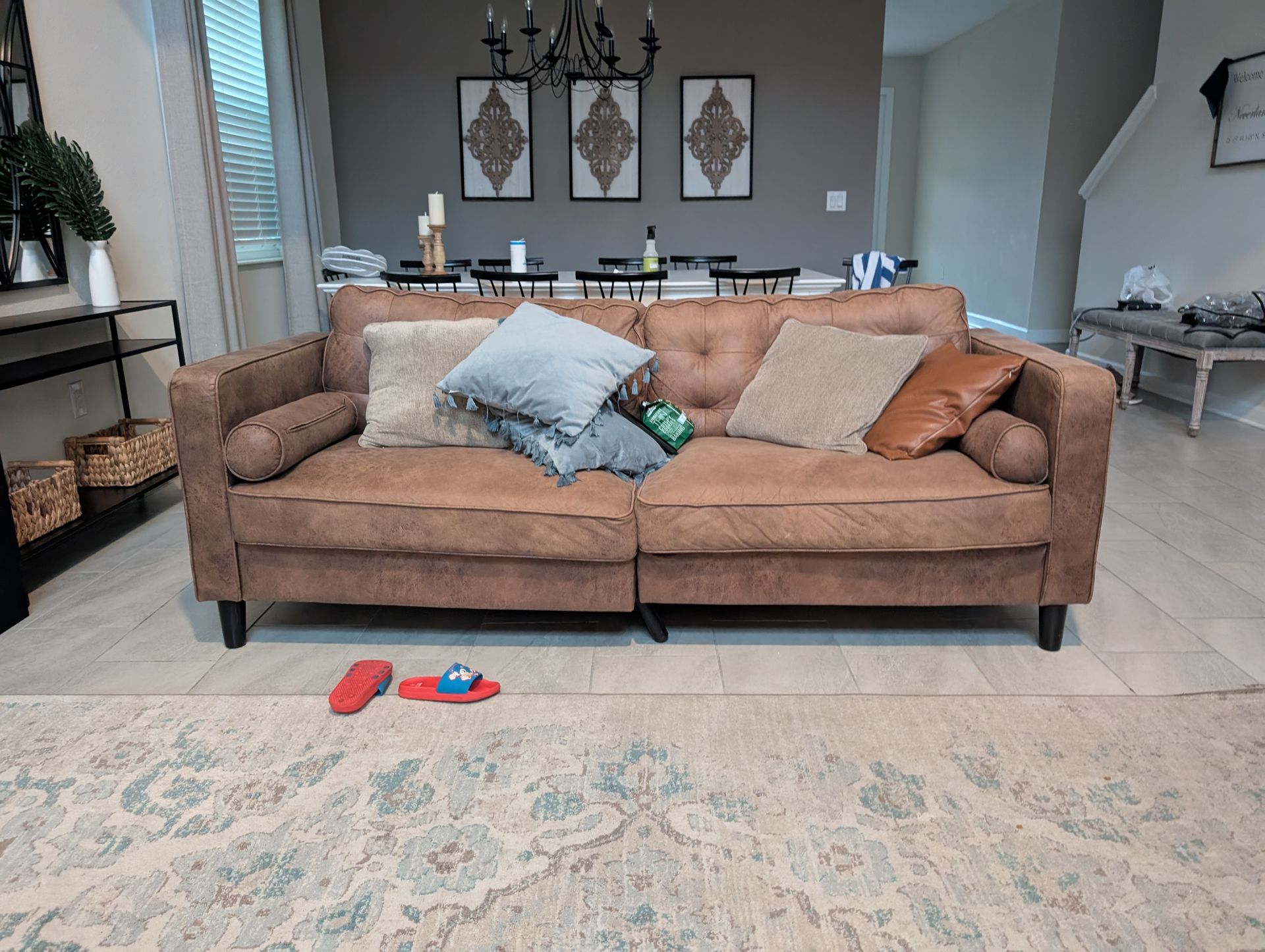 Brown couch with pillows in a living room, rug in front, toys on floor.