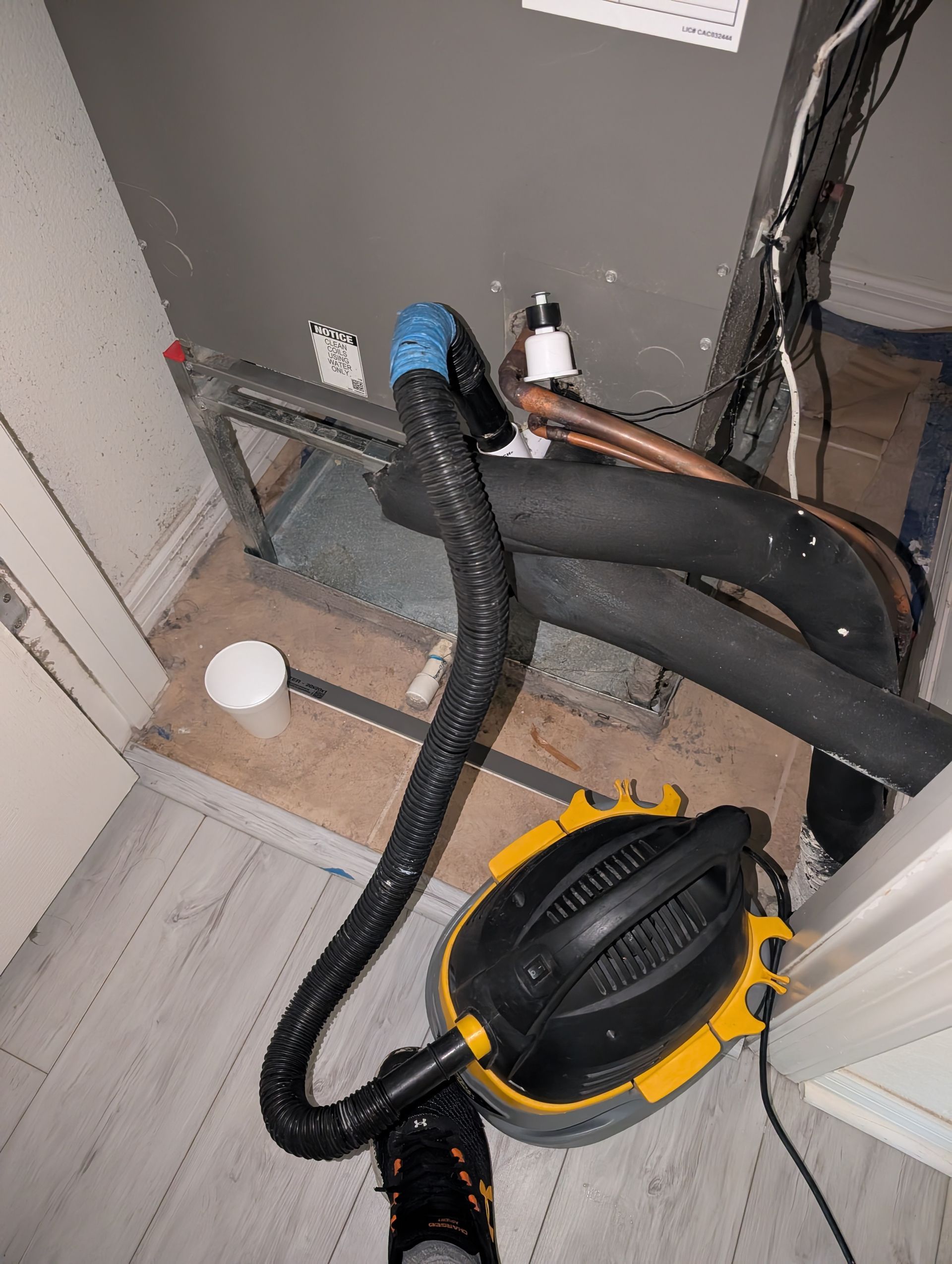 Yellow and black vacuum connected to HVAC system with black tubing in a utility room.