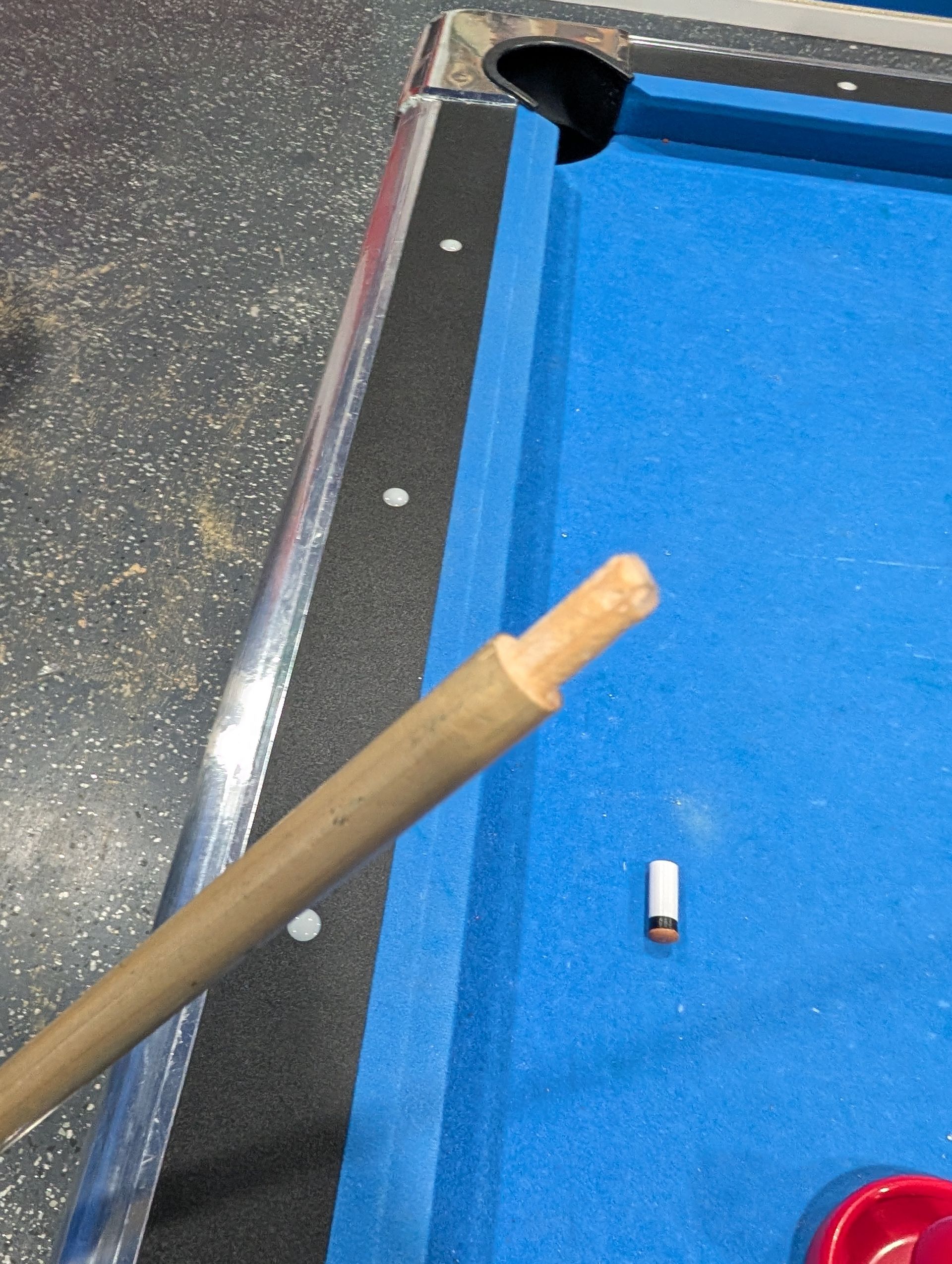 Broken pool cue on a blue pool table, showing the tip and ferrule detached.