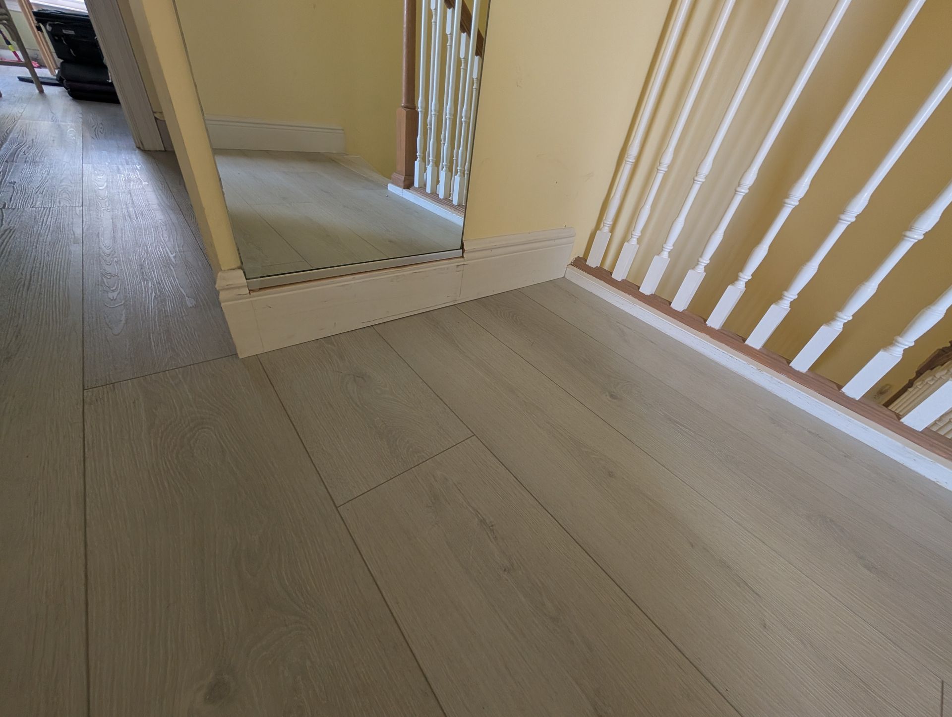 Light gray wood-look flooring and white trim along a staircase with a mirrored wall.
