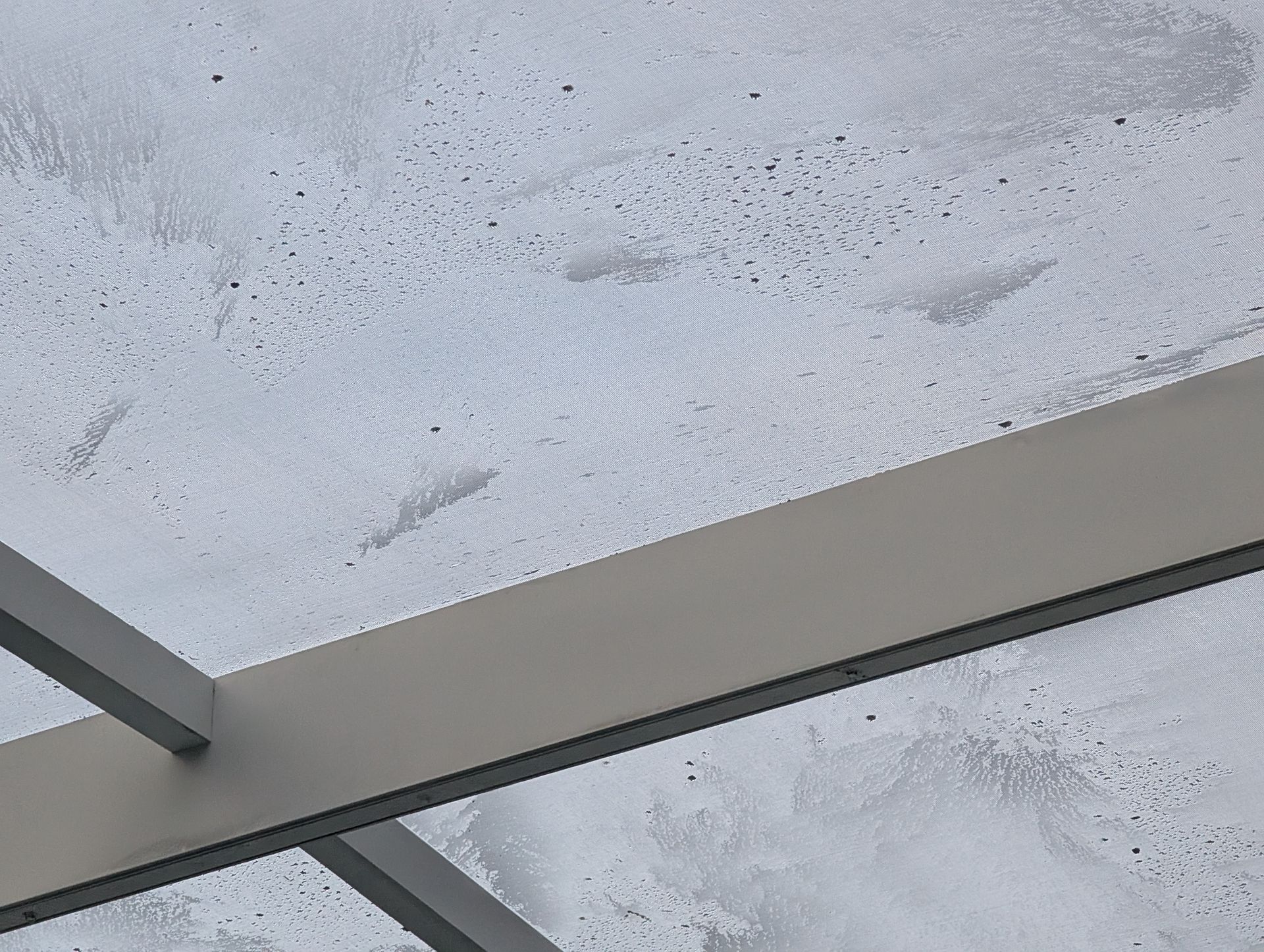 Gray metal beams supporting a white, textured ceiling with dark spots, viewed from below.