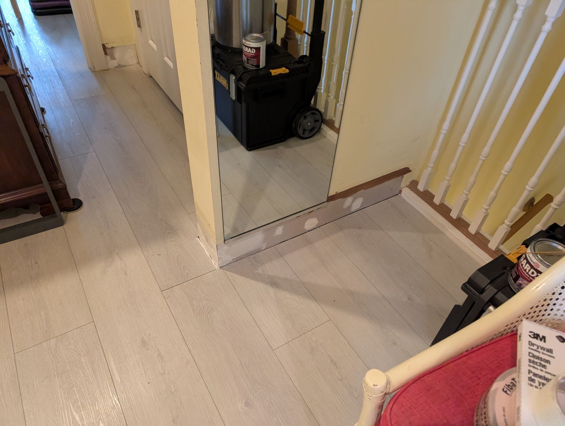 White painted wood floor in a hallway, with a mirror, stairs, and a tool case.