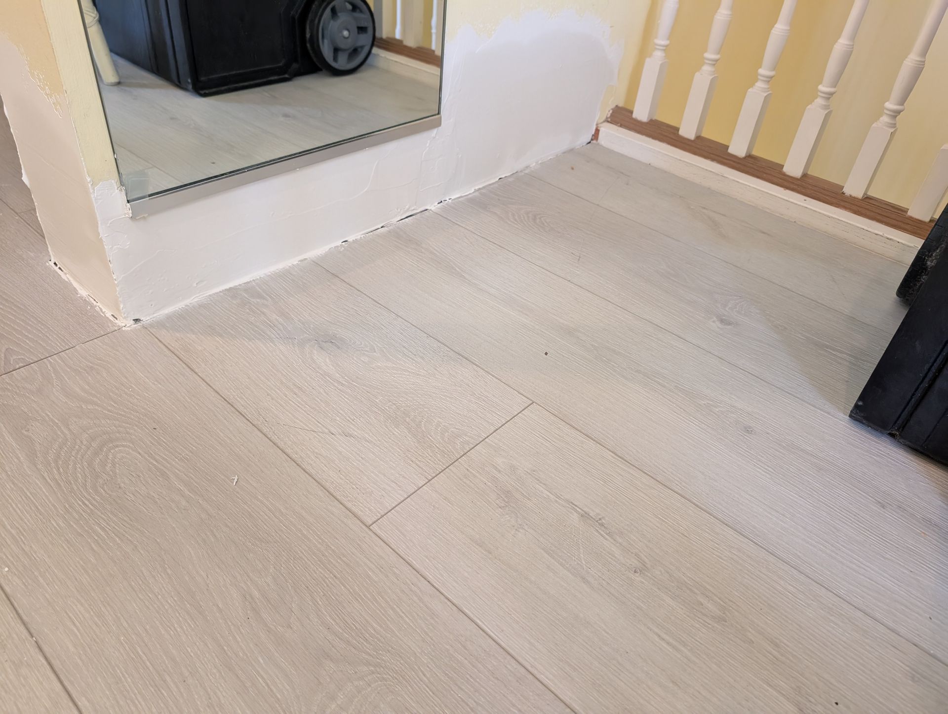 Light wood-look flooring in a hallway with a mirror, stairs, and a wheeled black object.
