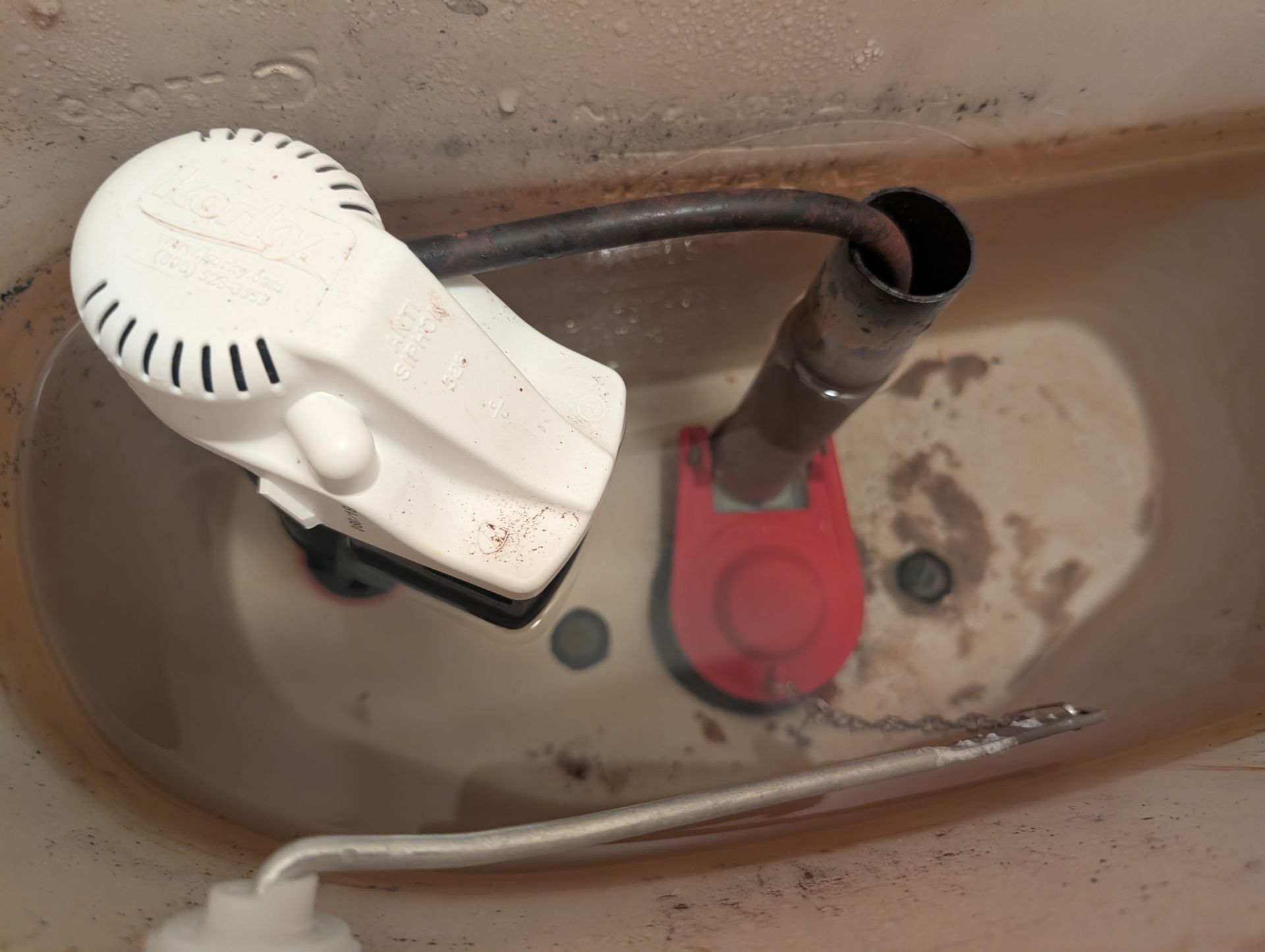 Toilet tank interior: a white fill valve, red float, and a metal fill tube.