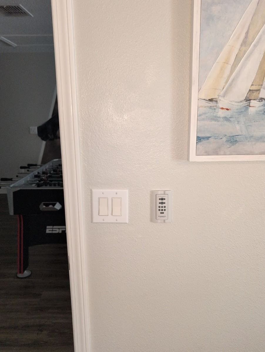 Light switches and thermostat on a light gray wall, painting of sailboats above.