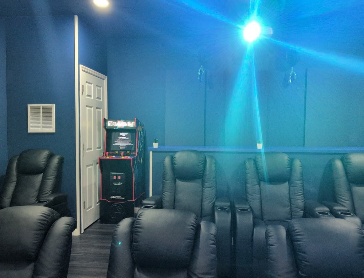 Dark blue home theater with recliners, arcade game, and bright projector light.