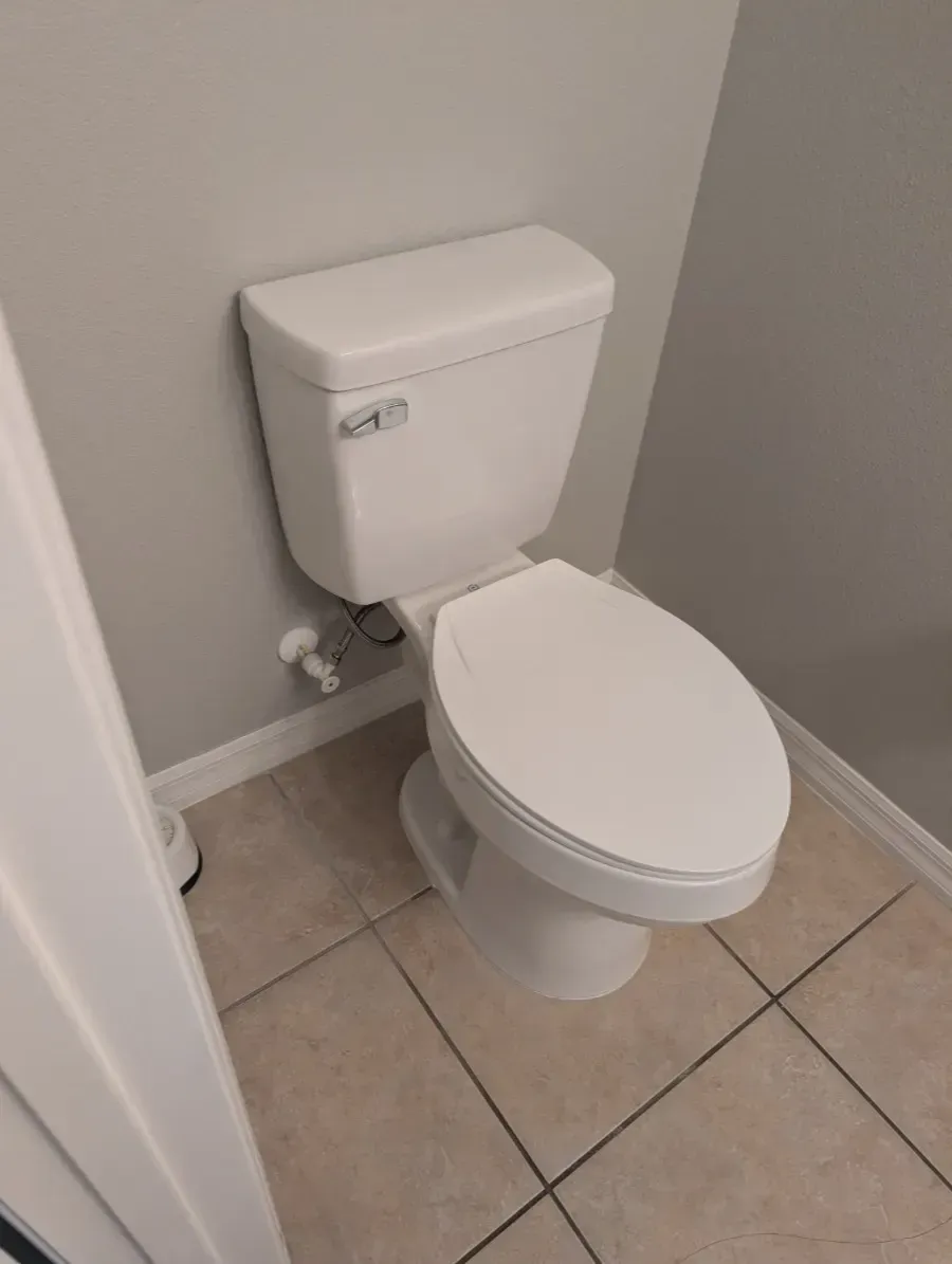 White toilet in a small bathroom with gray walls and beige tile flooring.