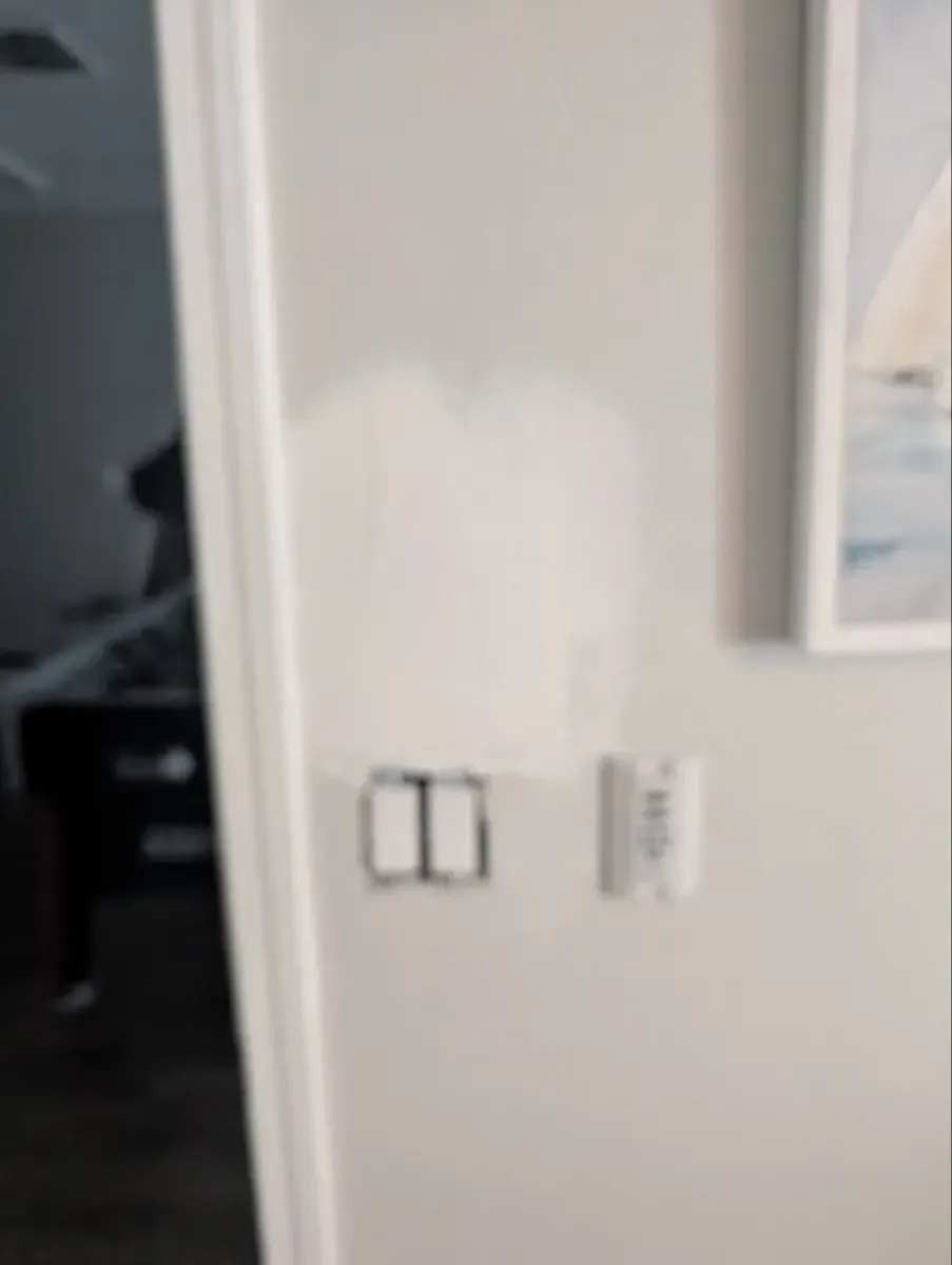 Light-colored wall with light switches and thermostat. Patch of paint above the switches.