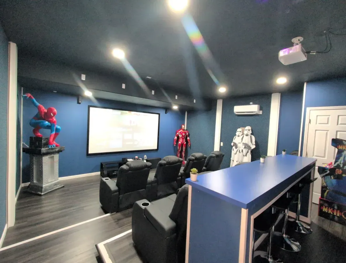 Home theater with superhero statues: Spider-Man, Iron Man, Stormtrooper, blue walls, projector screen, seating, bar.