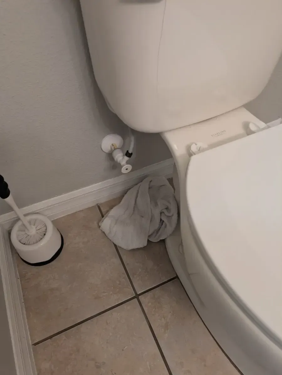 White toilet, close to wall, water shutoff visible, toilet brush on floor.