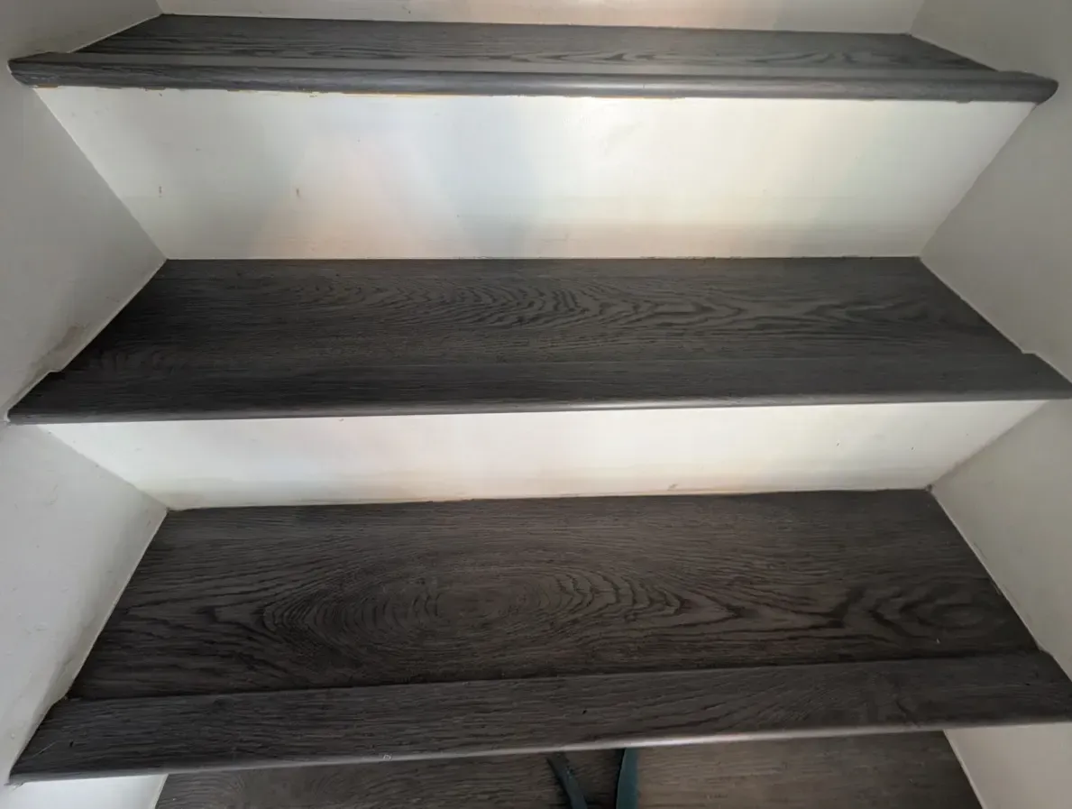 Wooden stair treads with white risers. Dark wood treads against a white wall.