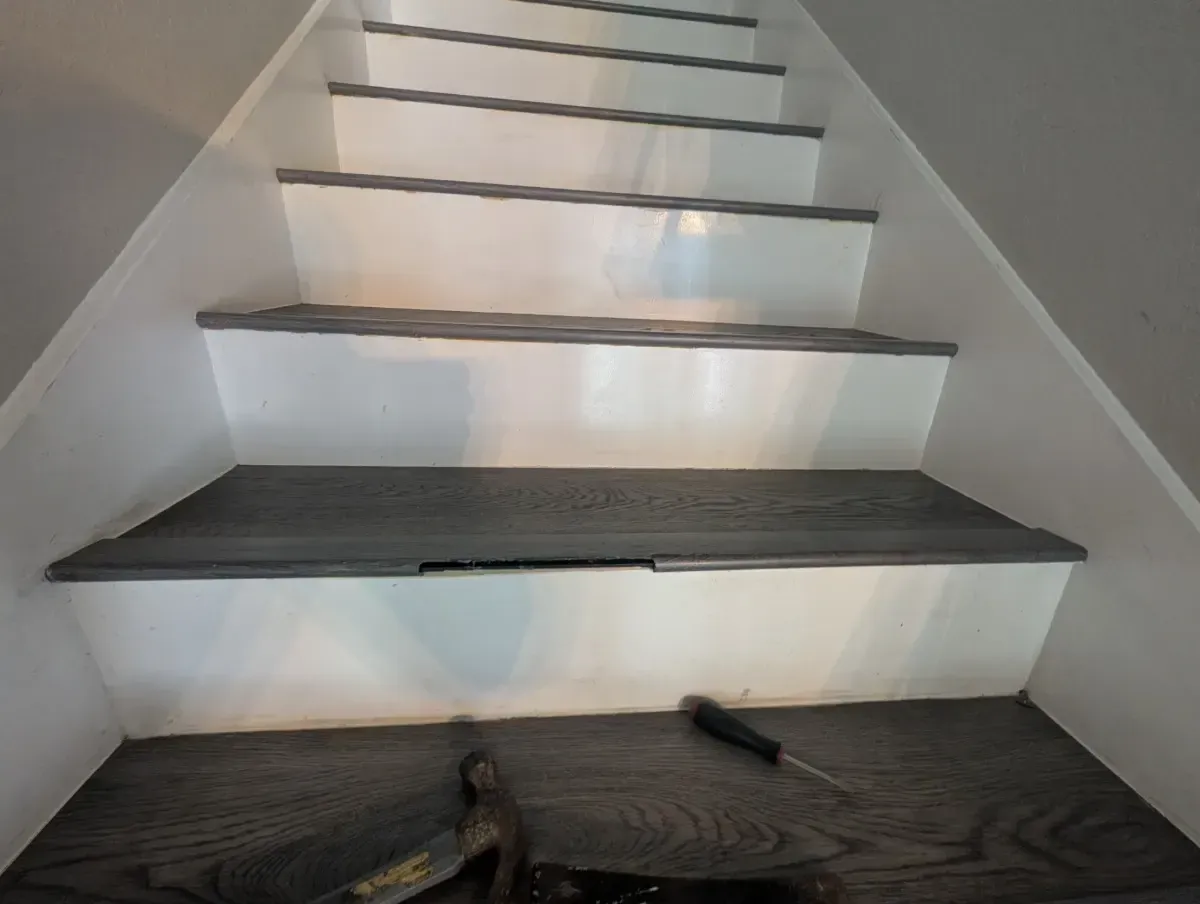 Staircase with gray treads, white risers. Repair tools visible at base; crack in tread.