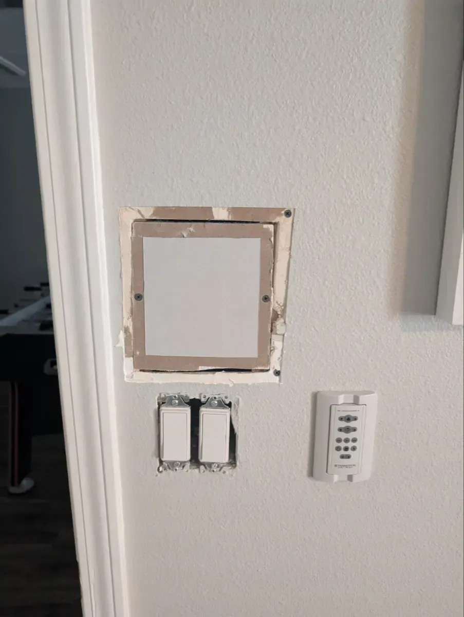 A wall with a blank square, light switches, and a thermostat.