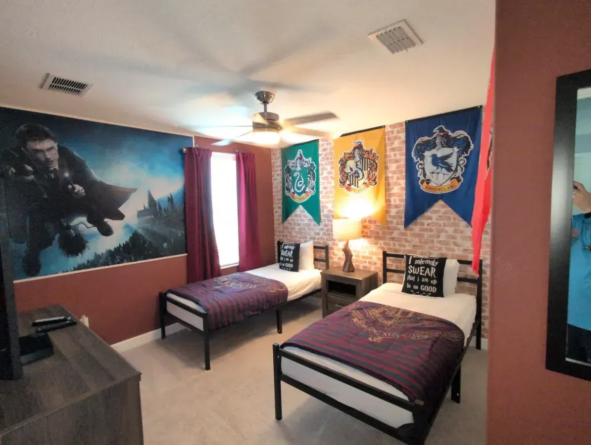 Harry Potter-themed bedroom with two twin beds, Hogwarts house banners, and a wall mural of a wizard.