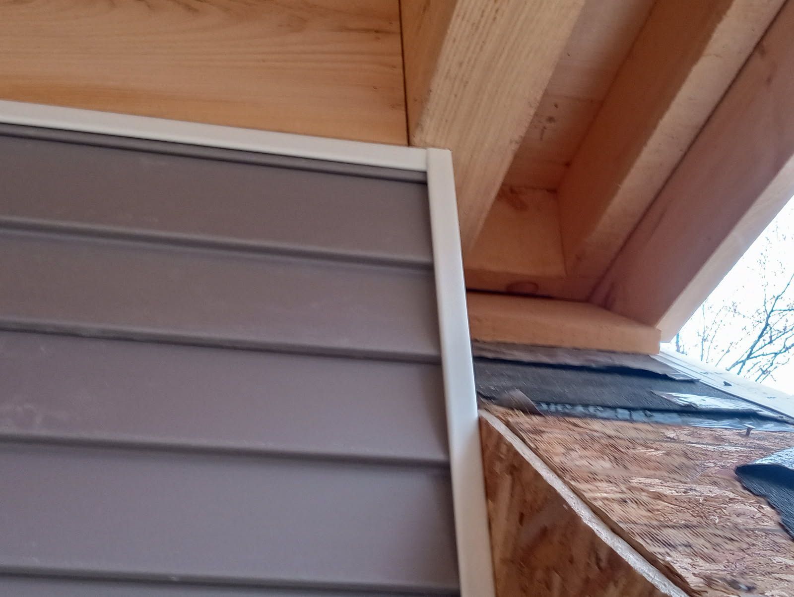 Gray siding with white trim, near wooden beams and roofing.