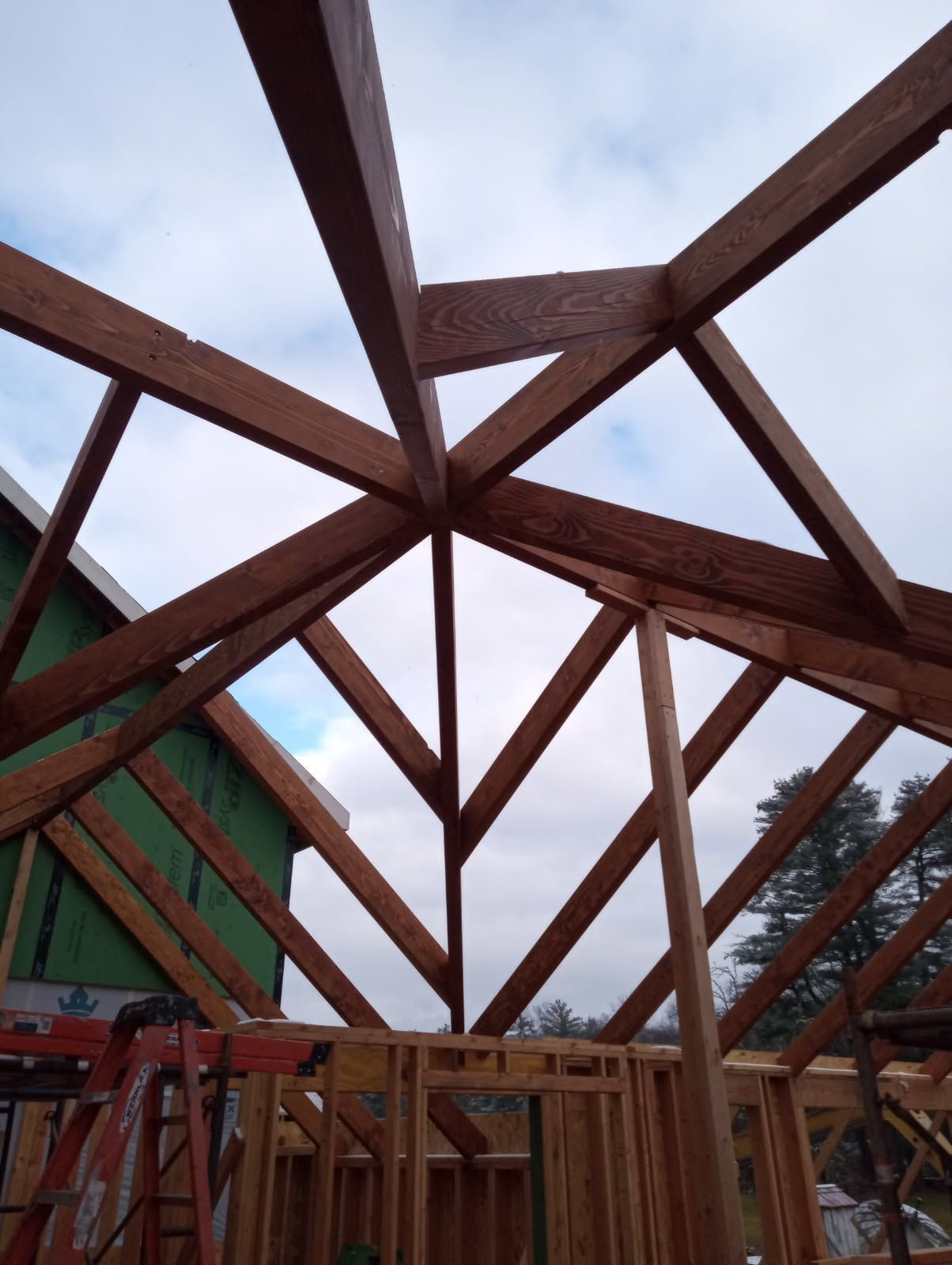 Wooden roof framework under construction against a cloudy sky.
