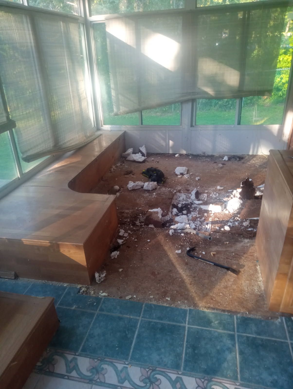 Sunroom interior, dirty. Wooden benches and tiled floor. Debris scattered on ground near window.