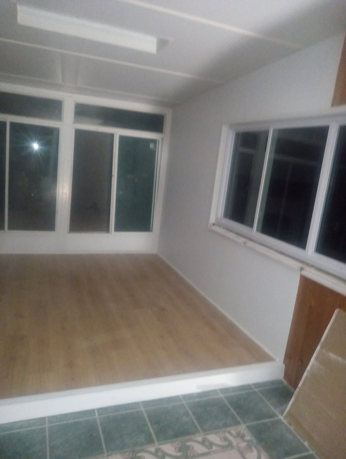 Empty room with wood flooring, white walls, and large windows.
