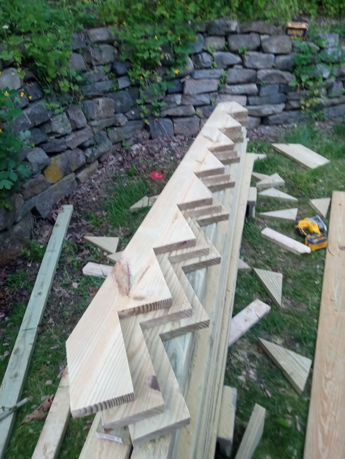 Wooden stair stringers being assembled outdoors near a stone wall.