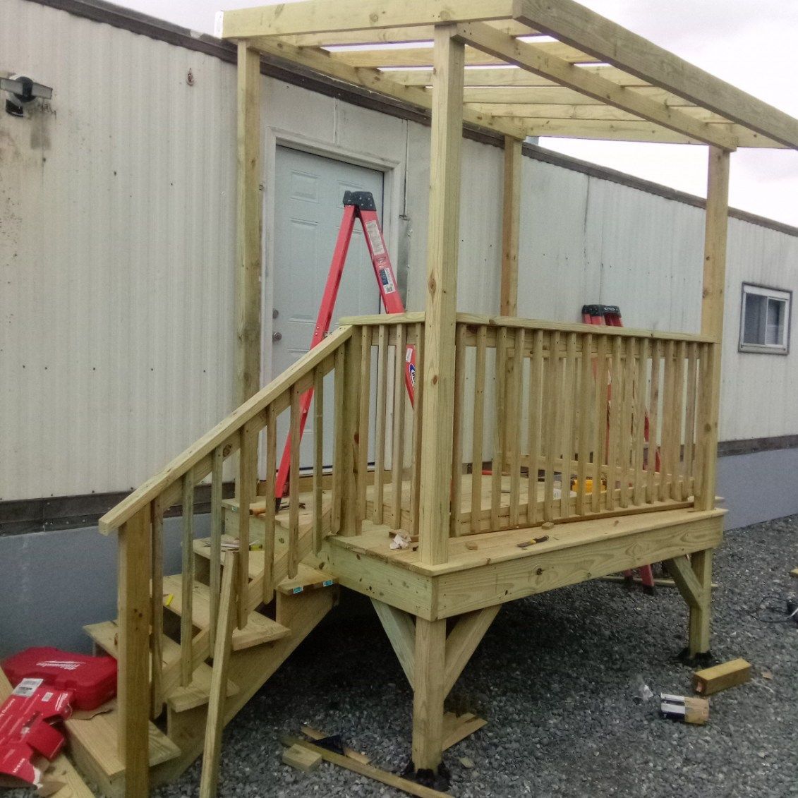 Wooden deck with stairs, handrails, and a small overhead structure built onto a white building.