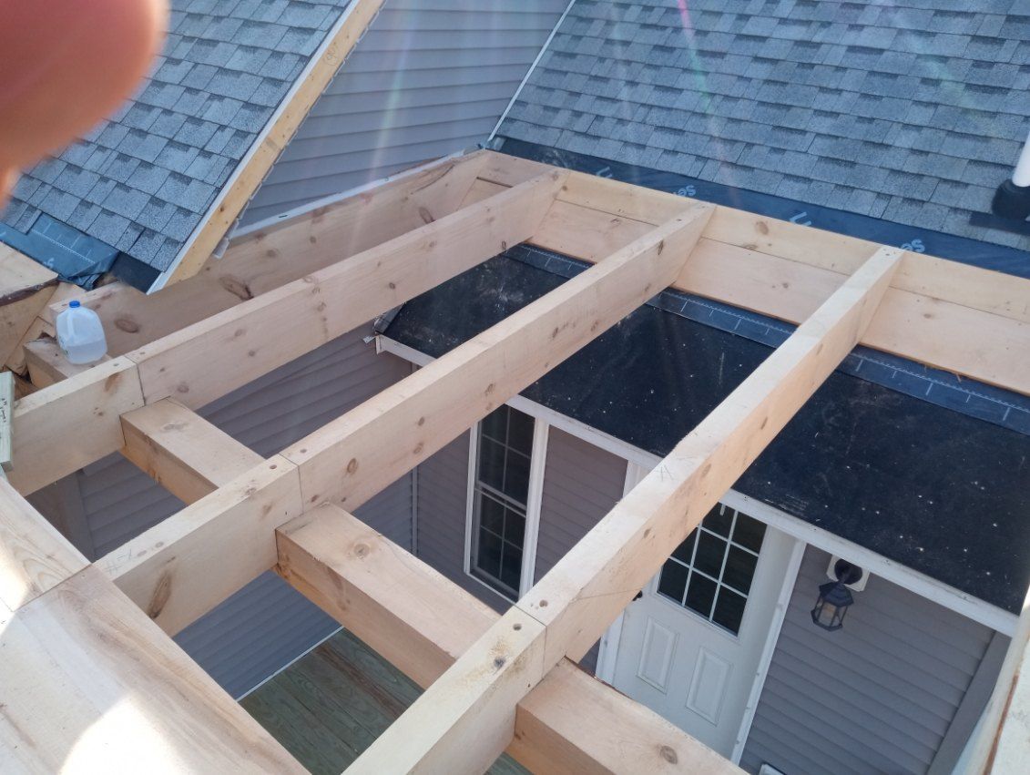 Wooden roof frame being constructed over an existing roof with blue shingles.