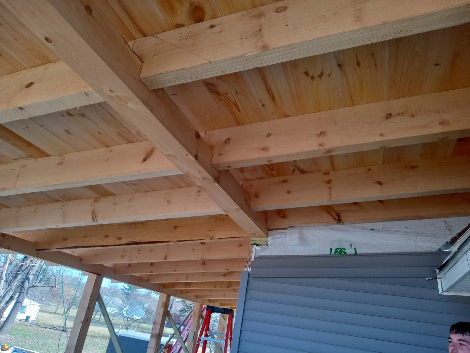 Wooden porch ceiling under construction, with exposed beams and plywood.