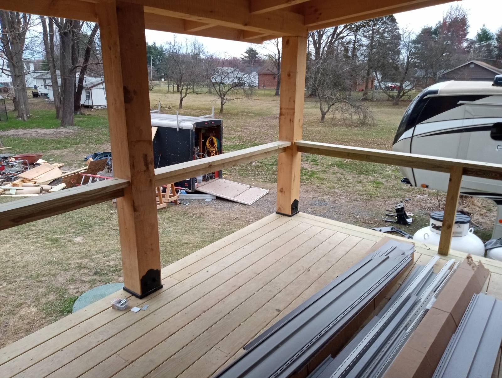 Wooden deck with railing, part of a gazebo. Outdoors, yard with camper in the background.