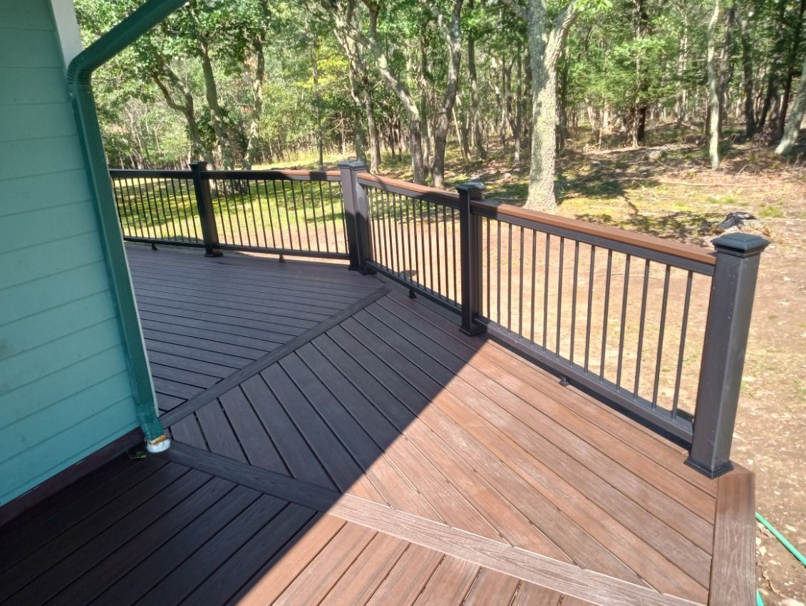 Composite deck with dark brown and light brown boards, black railing, surrounded by trees.
