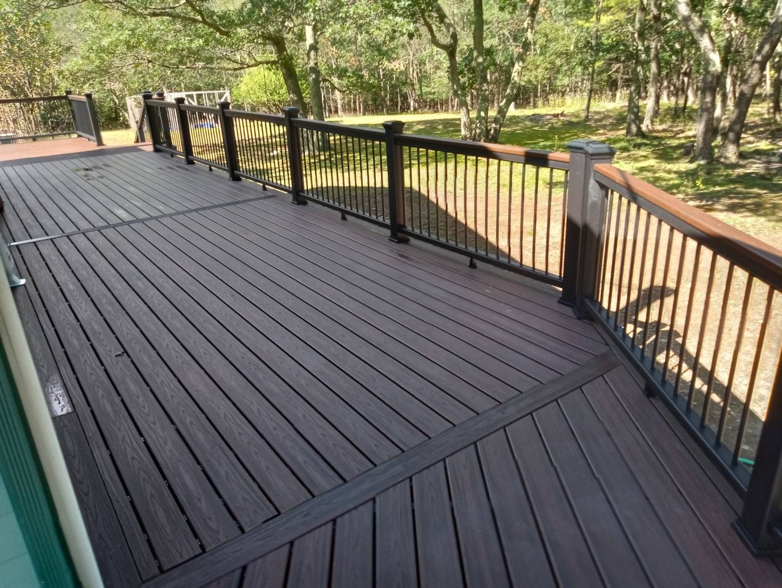Brown composite deck with black railing and wooded background.