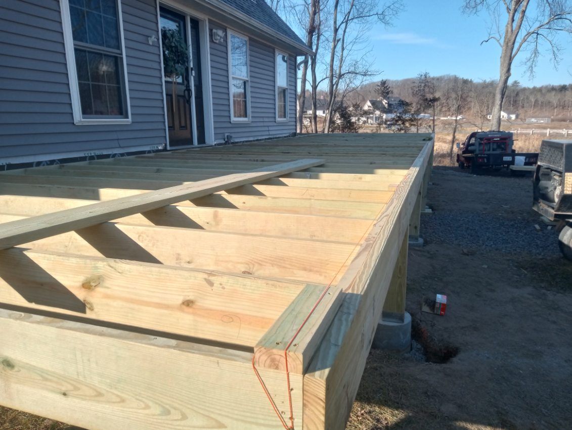A wooden deck under construction next to a house with blue siding.