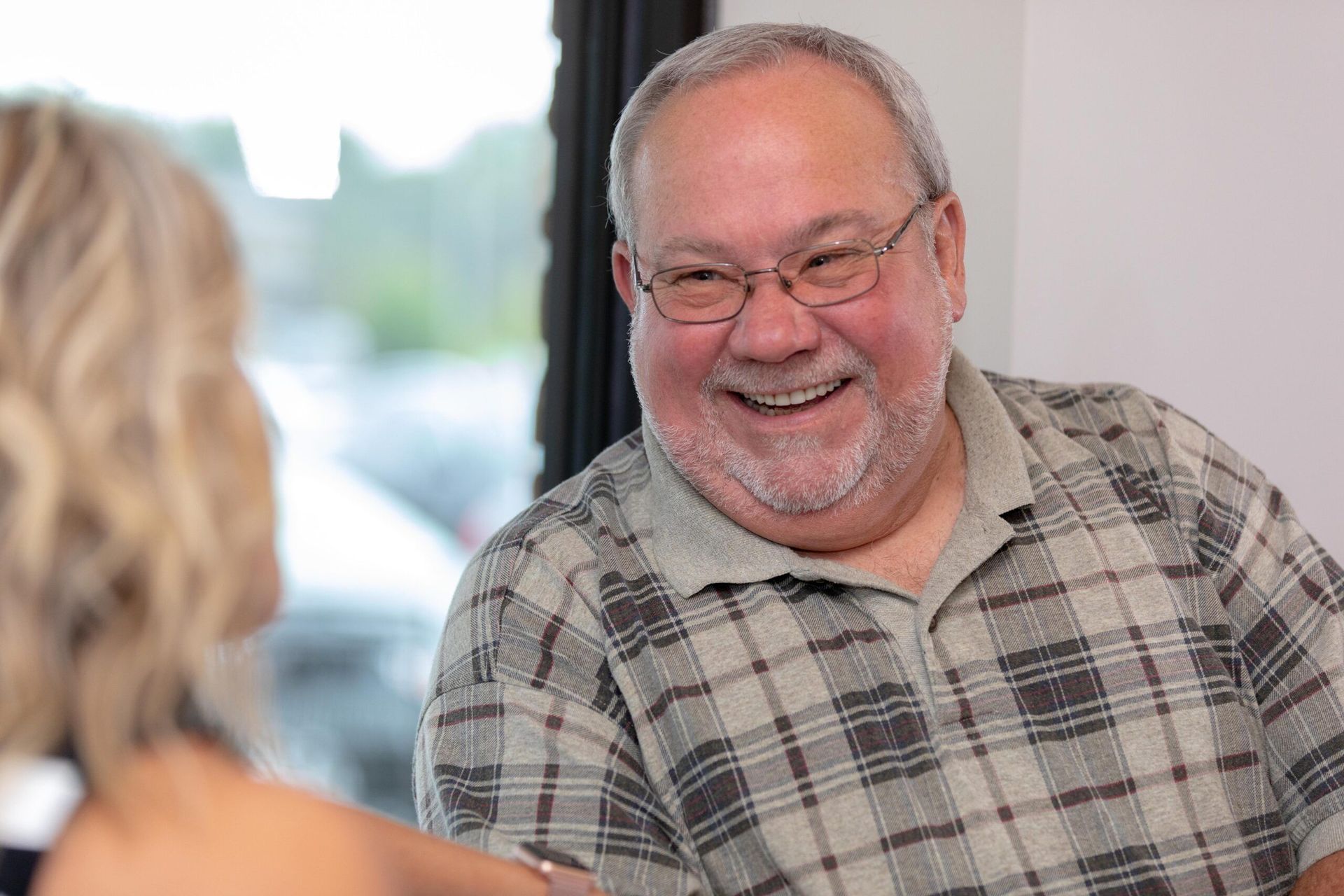 A man in a plaid shirt is smiling while talking to a woman.