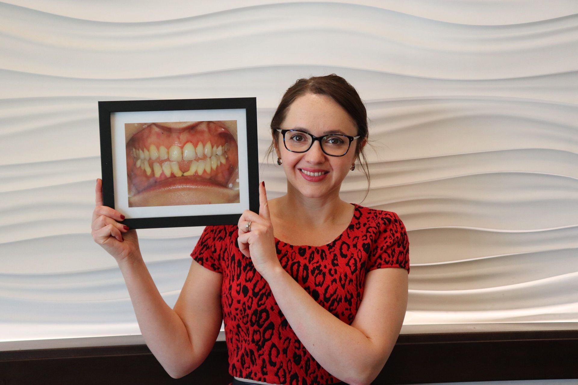 A woman is holding a picture of her teeth in a frame.