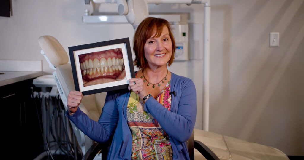 A woman is sitting in a dental chair holding a picture of her teeth.