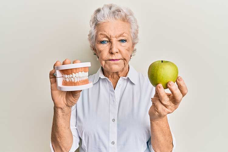 An elderly woman is holding a model of teeth and an apple.