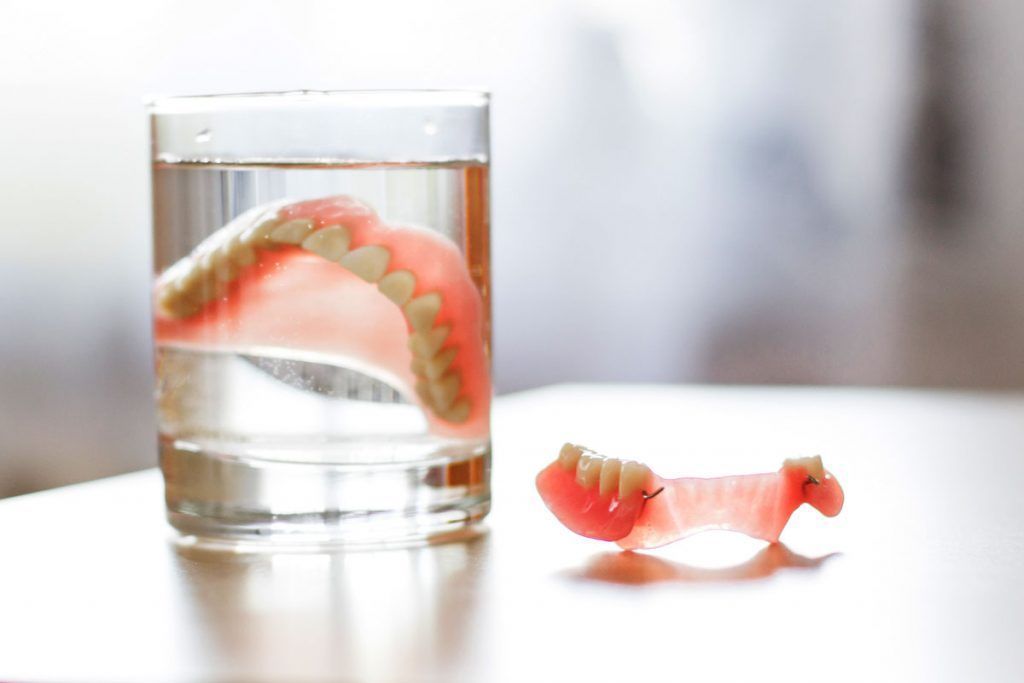 A denture is sitting next to a glass of water on a table.