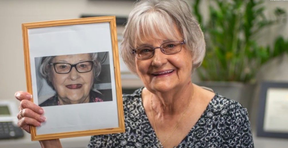 An elderly woman is holding a framed picture of herself.