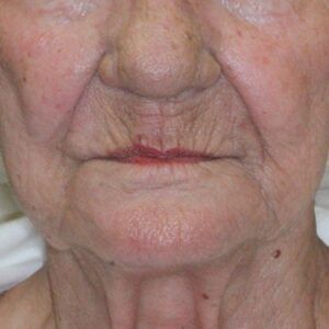 A close up of an elderly woman 's face with a red lip.