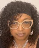 A woman with curly hair is wearing glasses and a headband.