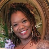 A woman with dreadlocks is smiling in front of a mirror.