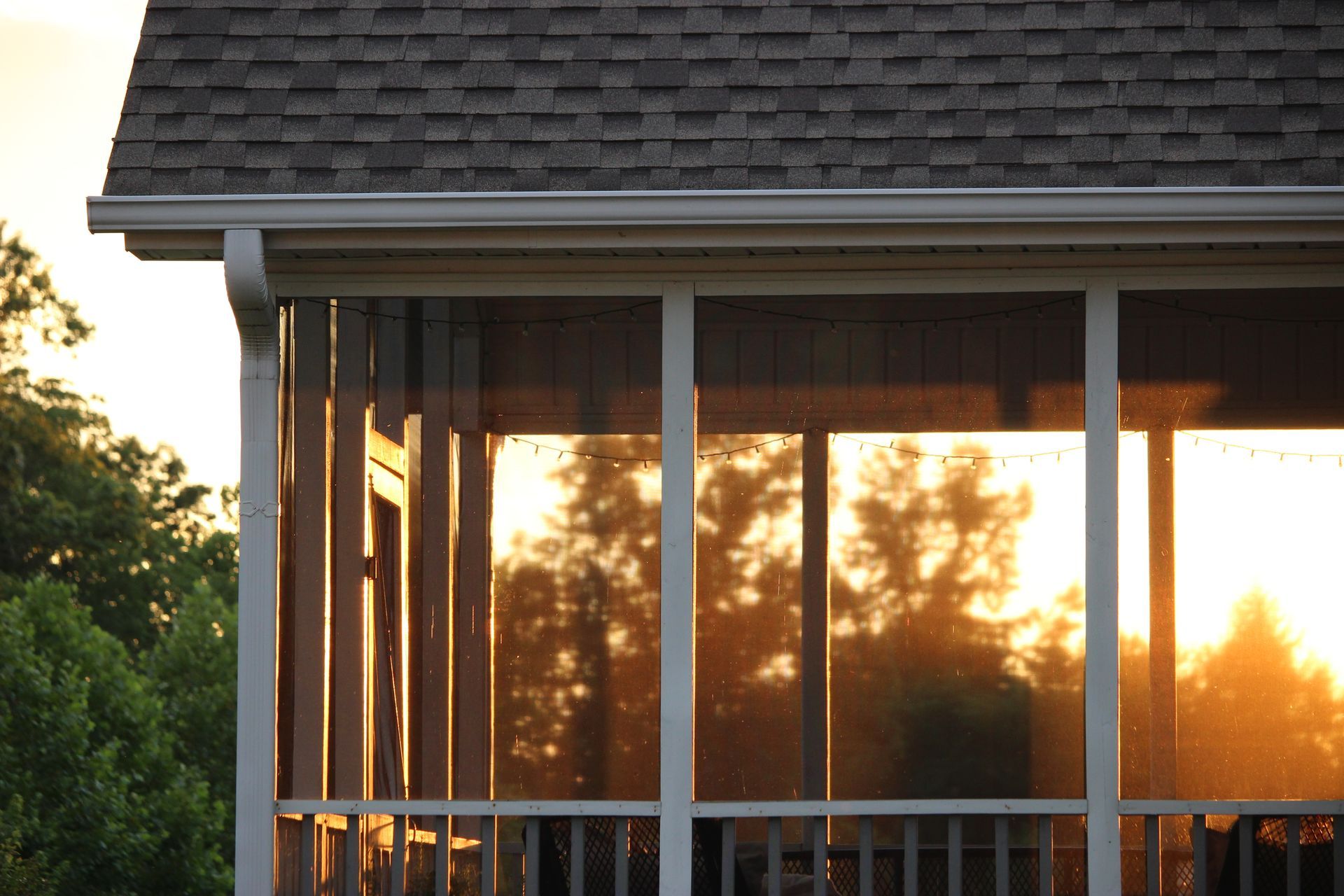 Sunlit screened porch with white railings and reflections of trees in the glass doors