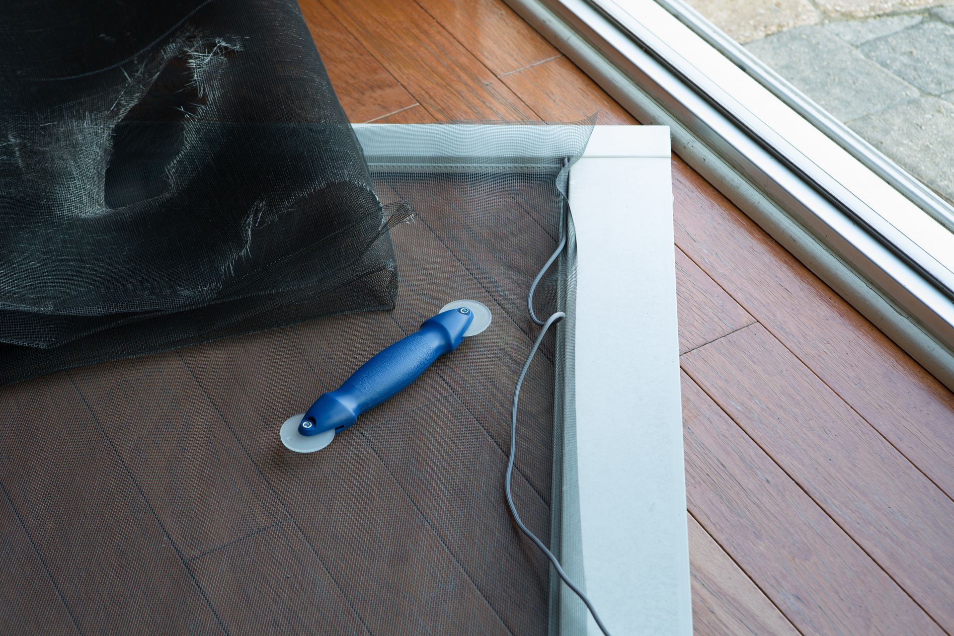 Blue-handled tool on a floor by a window and white baseboard