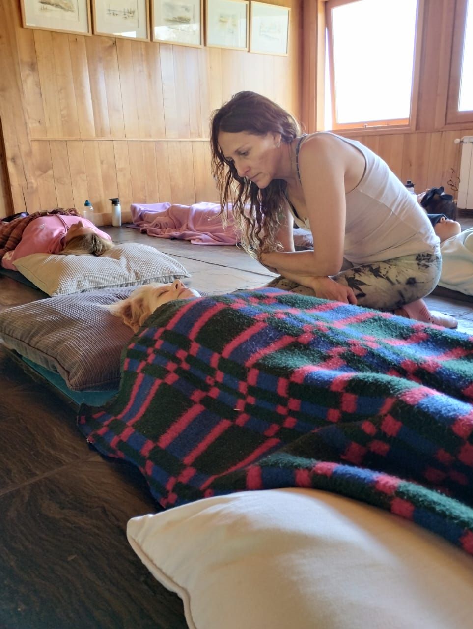 Una persona se arrodilla junto a otra que yace sobre una estera, cubierta con una manta estampada.
