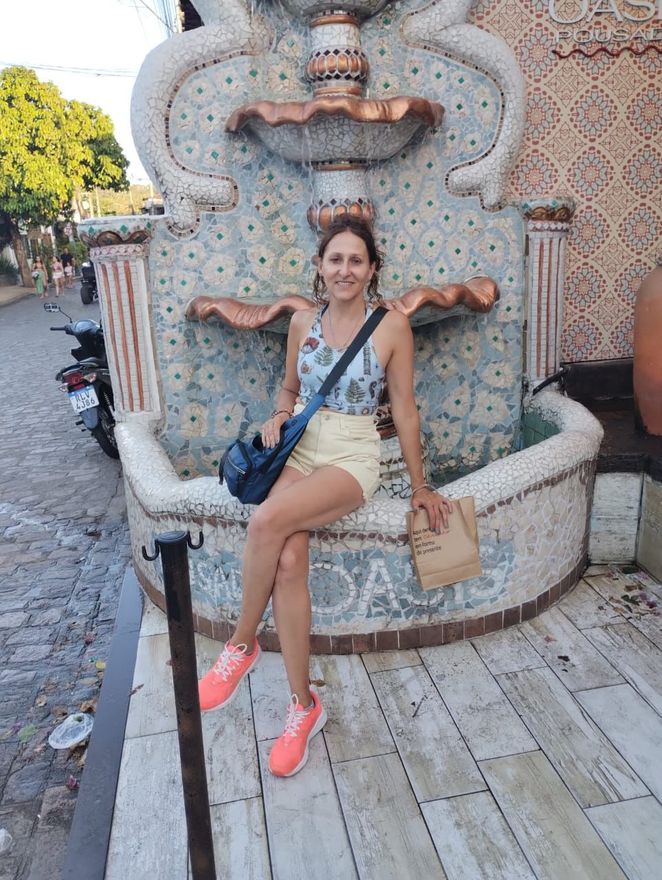 Una persona sentada en el borde de una fuente exterior de azulejos, vestida con una camiseta estampada.