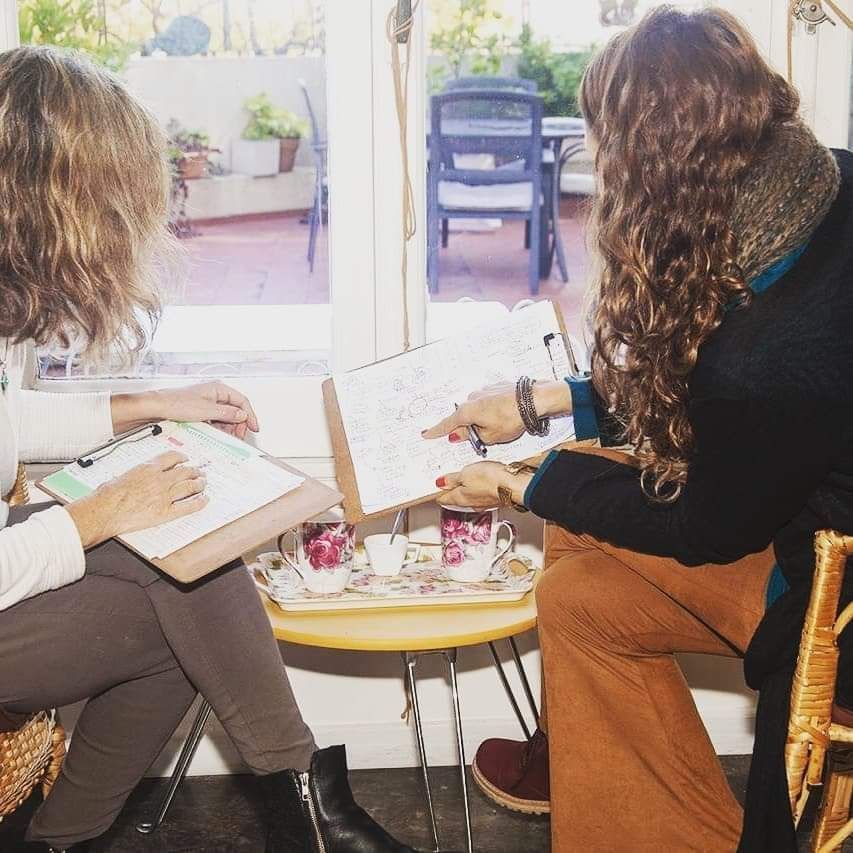 Dos personas están sentadas en una mesa pequeña en el interior, revisando documentos en portapapeles mientras toman el té.