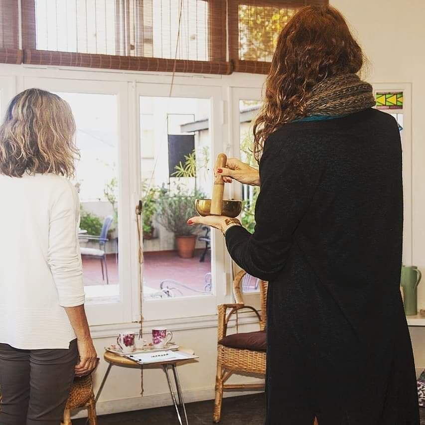 Una persona sostiene un cuenco tibetano y una baqueta mientras mira a otra persona.