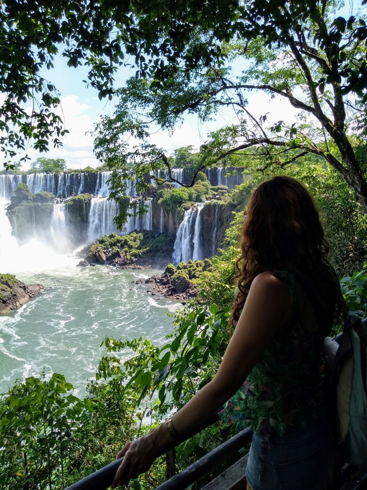 Una persona se encuentra de pie junto a una barandilla, contemplando una amplia cascada.
