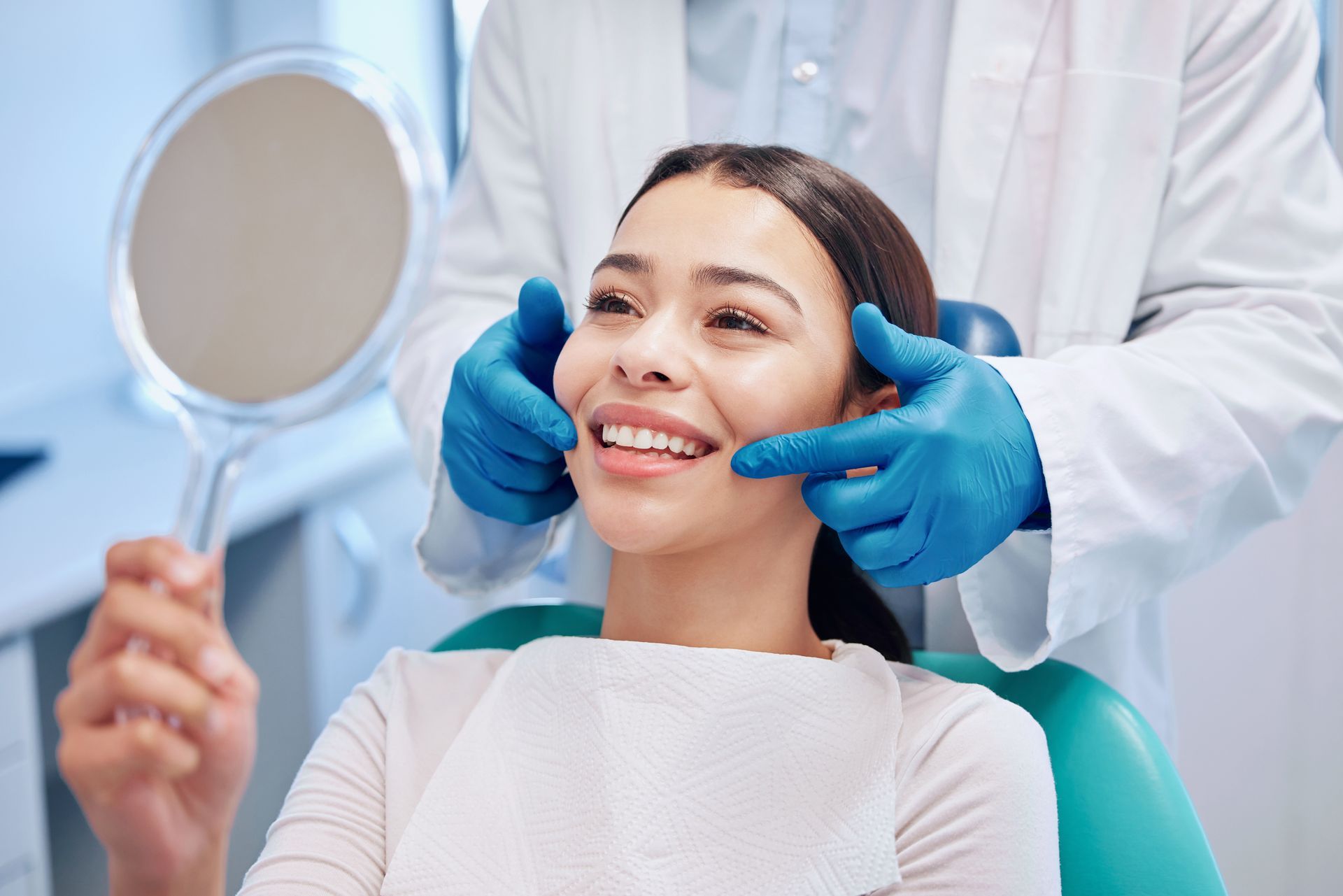 Dental patient holding a mirror while a dentist examines facial symmetry during a consultation. Dental patient holding a mirror while a dentist examines facial symmetry during a consultation.