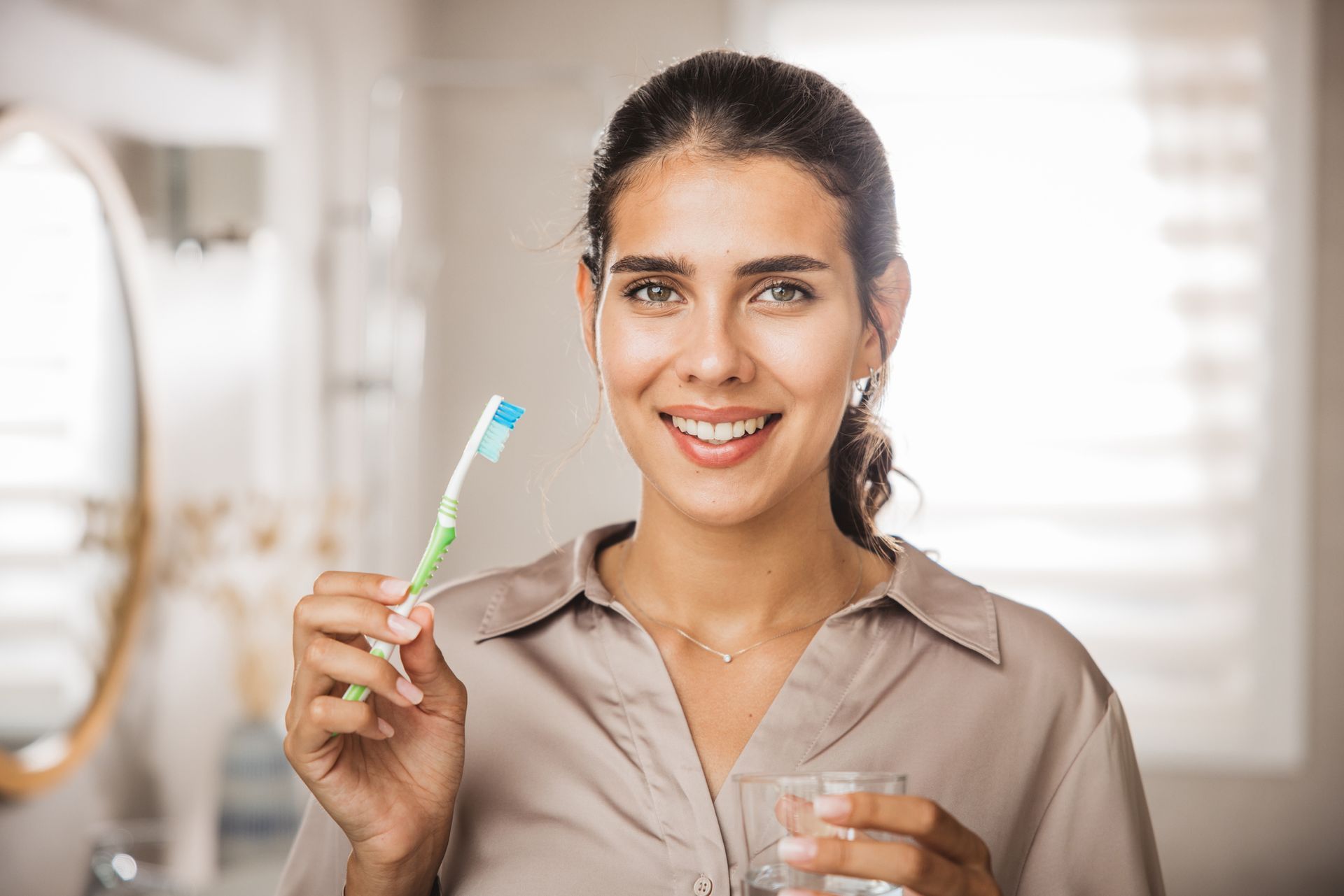 Smiling person holding a toothbrush and glass of water in a clean bathroom. Smiling person holding a toothbrush and glass of water in a clean bathroom.