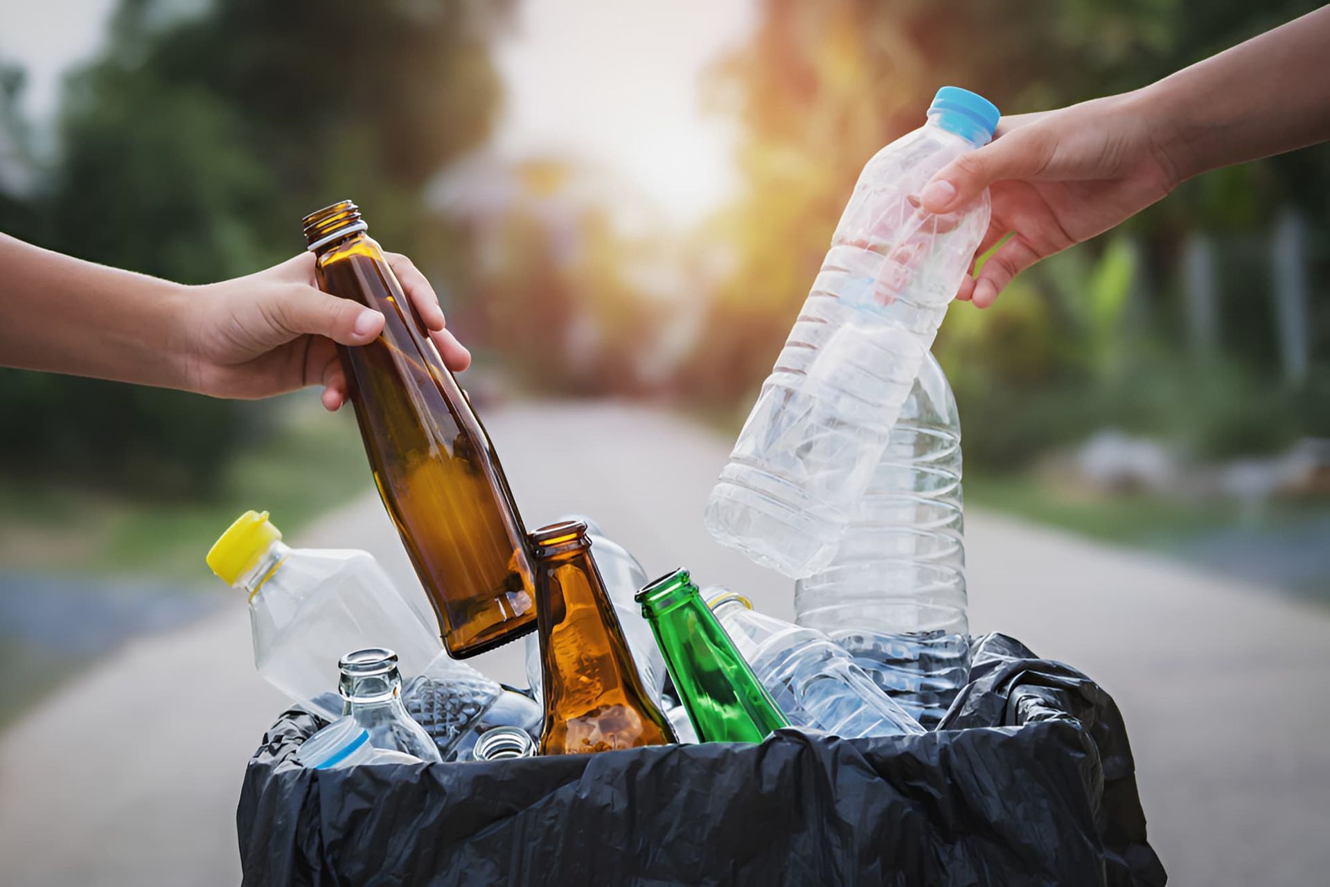 A Person Is Throwing Bottles And Plastic Bottles Into A Trash Can — North Queensland Recycling Agents In Bungalow, QLD